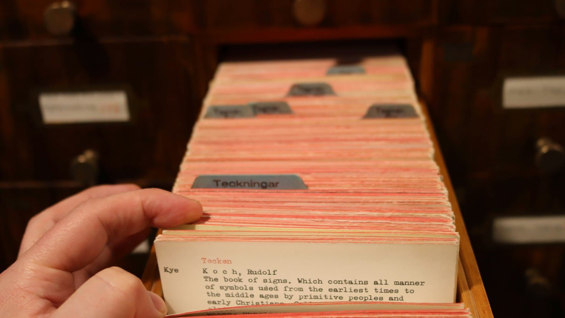 Eine Hand blättert in einem Karteikasten mit beschrifteten Registerkarten, Sinnbild für eine geordnete Wissensdatenbank